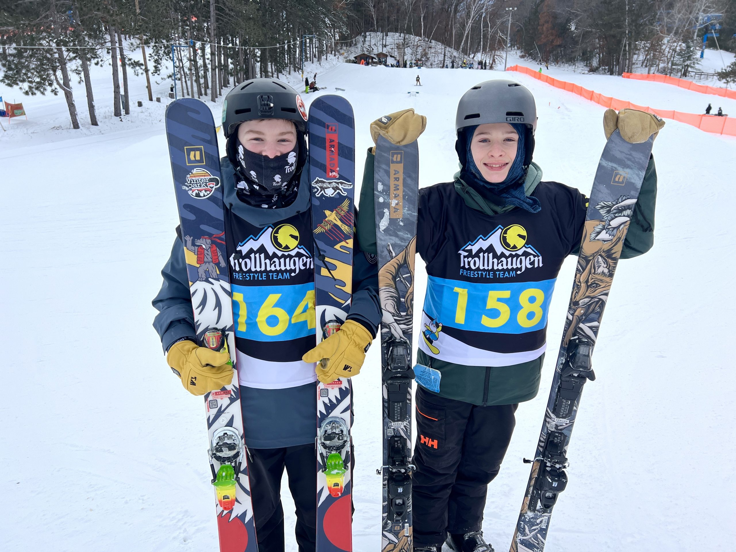 Photo of two skiers posing with their skiis and the Trollhaugen hills in the background